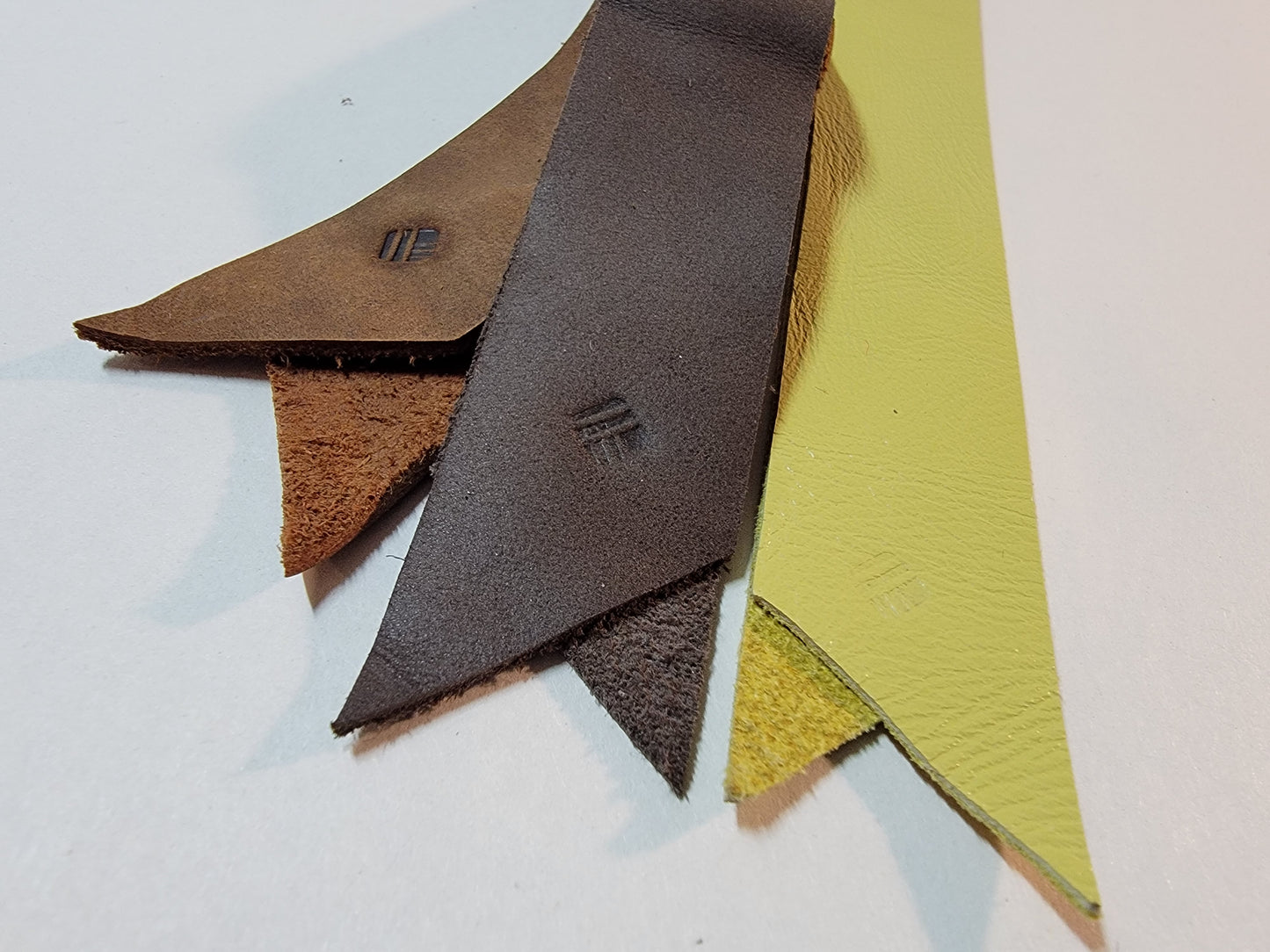 A close-up of three Sewnota Standard bookmarks, one light brown, one grey-brown, and one yellow-green. They all show a heat-stamped logo for mstlo (Malcolm Stielow)