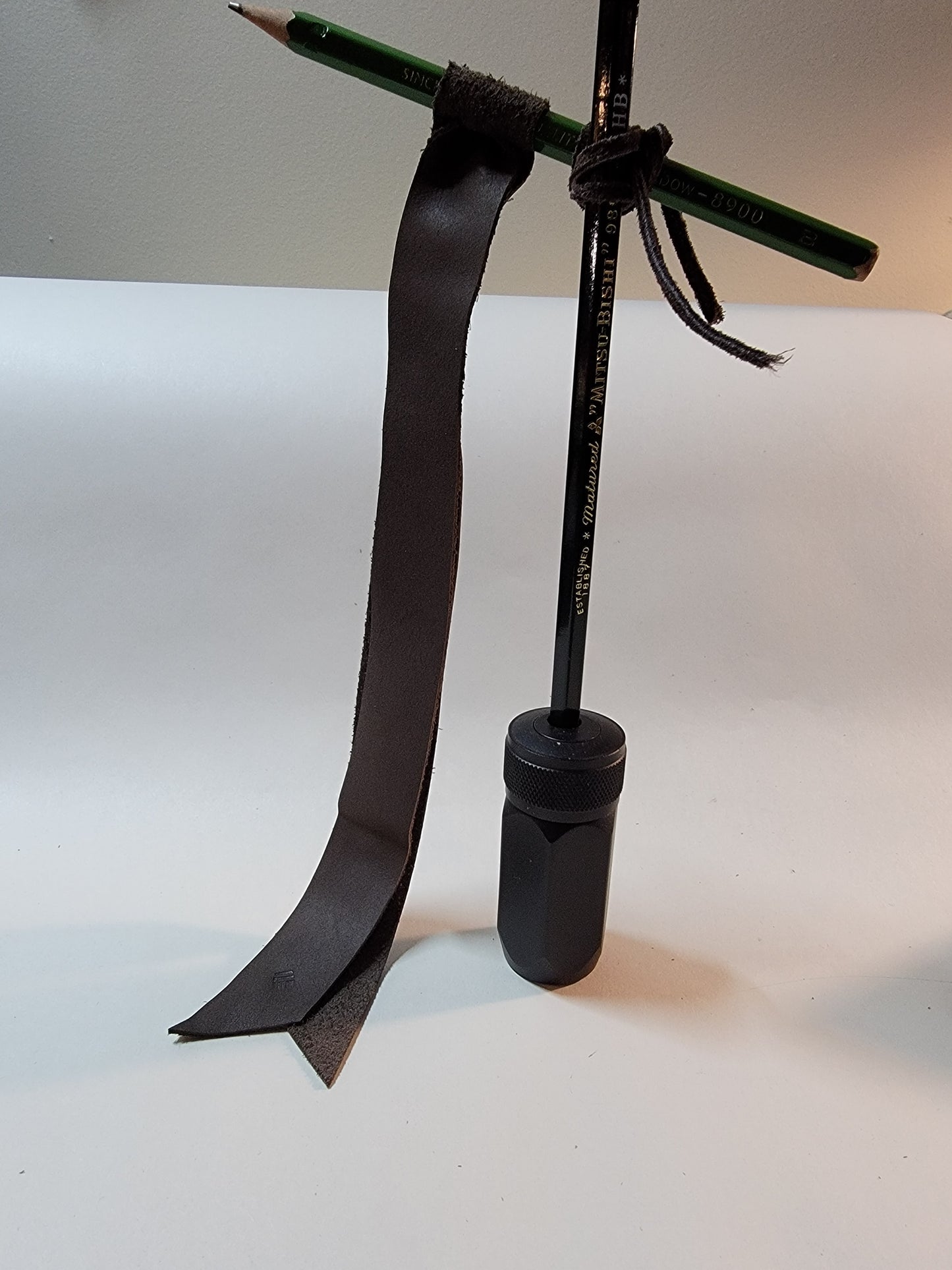 A grey-brown Sewnota Standard bookmark on a t-shaped flagpole made out of pencils. A Blackwing pencil sharpener serves as the flag pole stand.