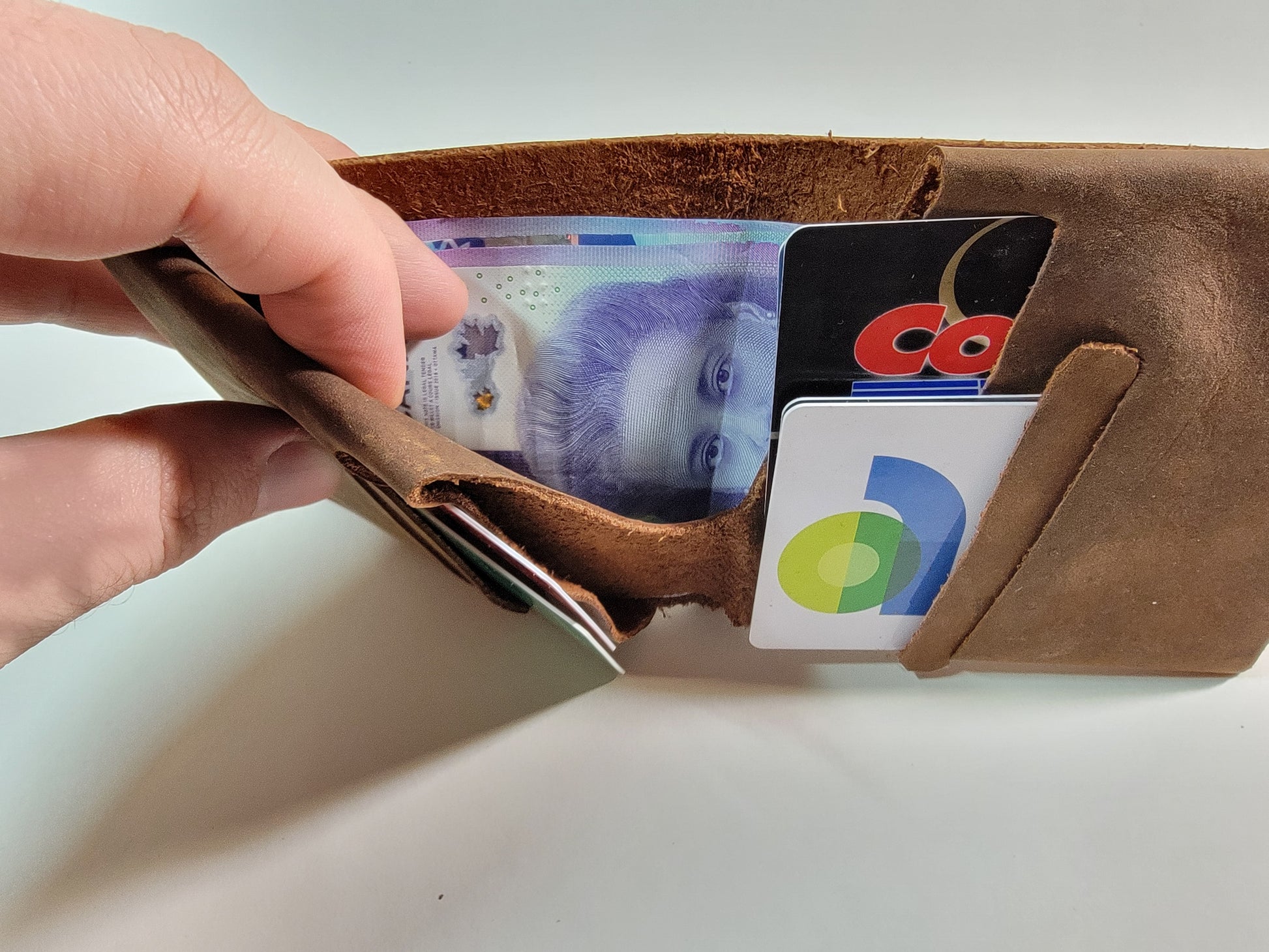 A hand holding a brown leather wallet from the side to show the pocket where bills are held.