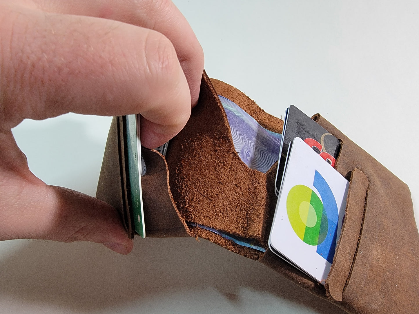 A hand holding a brown leather wallet from the side to show the pocket behind the card slots.