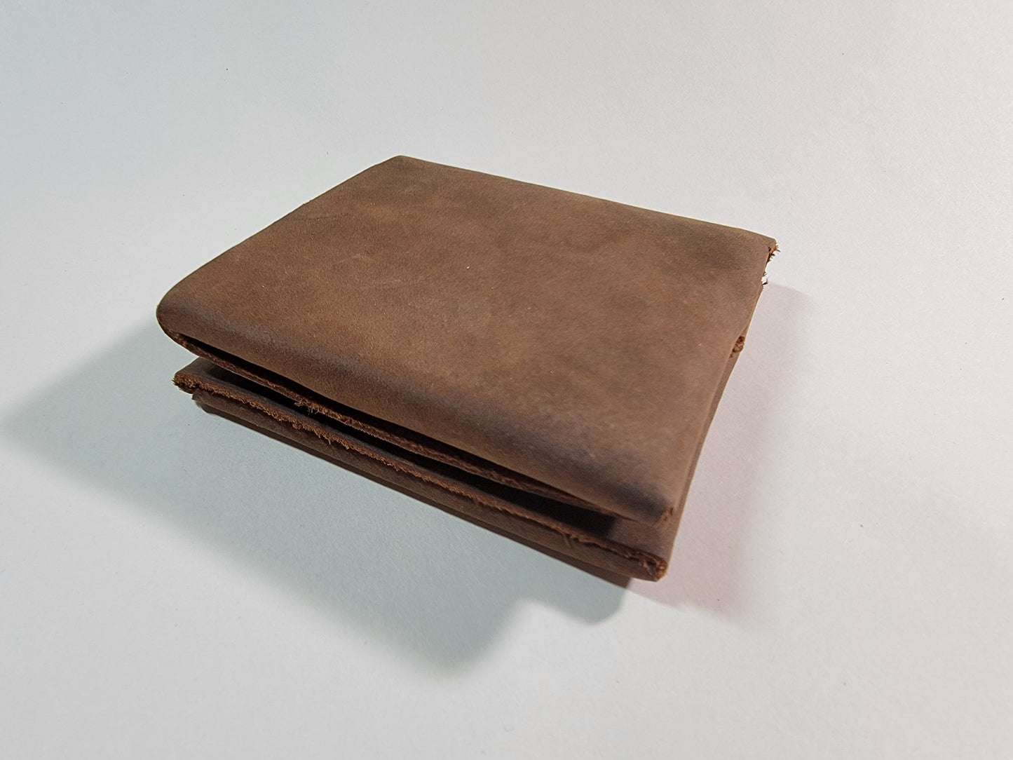 A closed, square, rough-cut brown leather wallet.